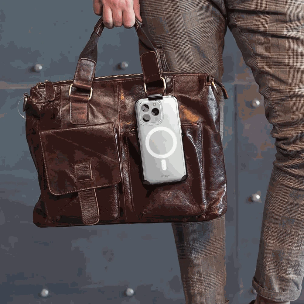 Clear iPhone 15 Pro Max case with holster attached to brown leather bag, showcasing durability and style.